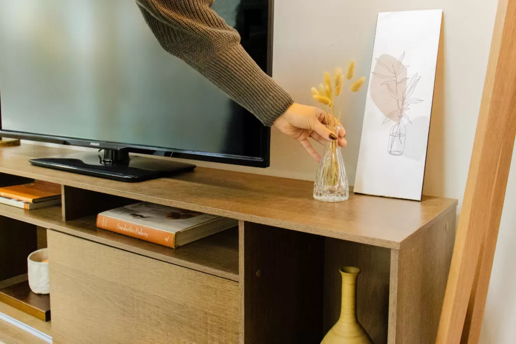 Rack em cores de madeira clara, com vaso de planta em cima, com televisão em cima e outros itens de decoração.