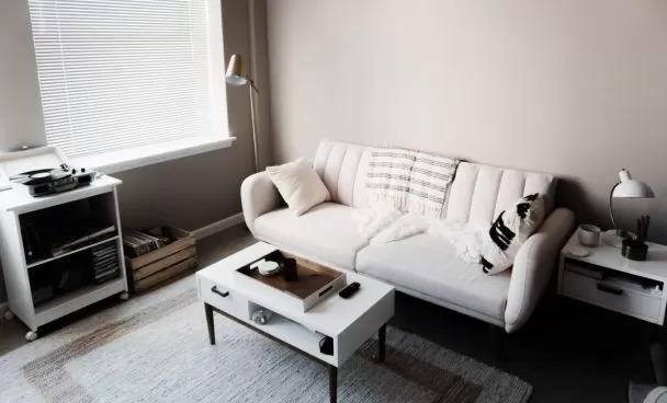 Sala de um apartamento pequeno decorada com sofá e mesa de centro brancos.