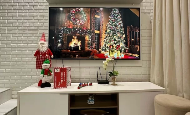 Sala de estar decorada para o Natal, com enfeites de Papai Noel, cartas de Natal e trem em miniatura em cima do rack.