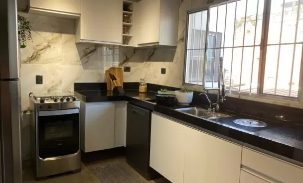 Pia em inox sobre bancada preta com portas brancas em frente a uma janela.