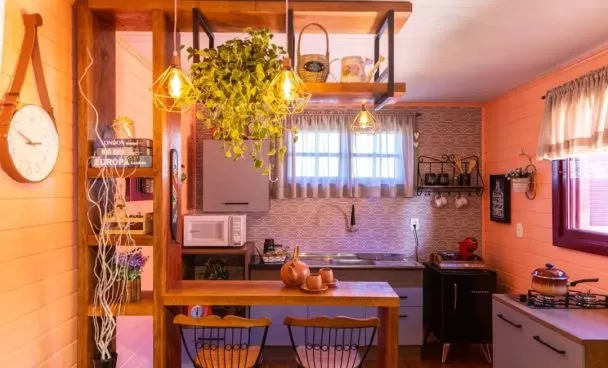 Cozinha Madesa, nas cores rustic e branco, com uma bancada e estante amadeirados e decorado com muitas plantas e cerâmicas.