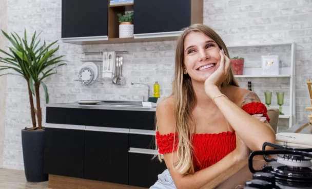 A imagem ilustra uma mulher loira de blusa vermelha no ombro na frente de uma cozinha planejada pequena, simples e barata.