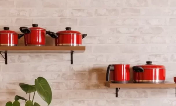 panelas vermelhas em diversos modelos estão dispostas sobre uma superfície escura em frente a um fundo branco, em conjunto com outros utensílios de cozinha