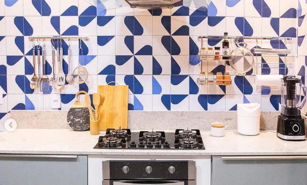 Cozinha Madesa Cinza com parede em azulejos azuis e brancos. Sobre a bancada clara, estão utensílios de uso diário.