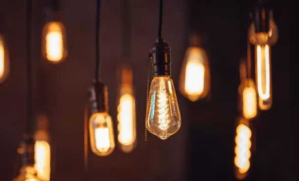 Várias lâmpadas de filamento estilo Edison penduradas, emitindo uma luz quente e amarelada em um ambiente escuro.