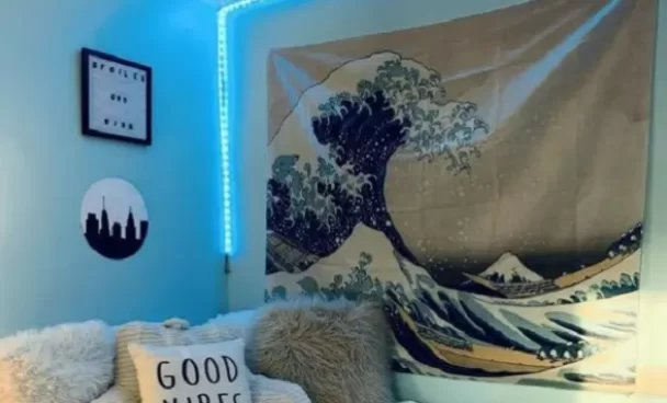 sala com sofá claro, mantas brancas e uma cortina com desenho de onas do mar. Na parede está uma fita de led azul que ilumina o ambiente.