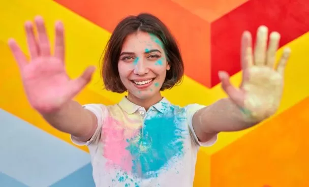 A imagem ilustra uma jovem de cabelo curto chanel em uma parede colorida e com as mãos pintadas de tinta simbolizando a pintura geométrica.